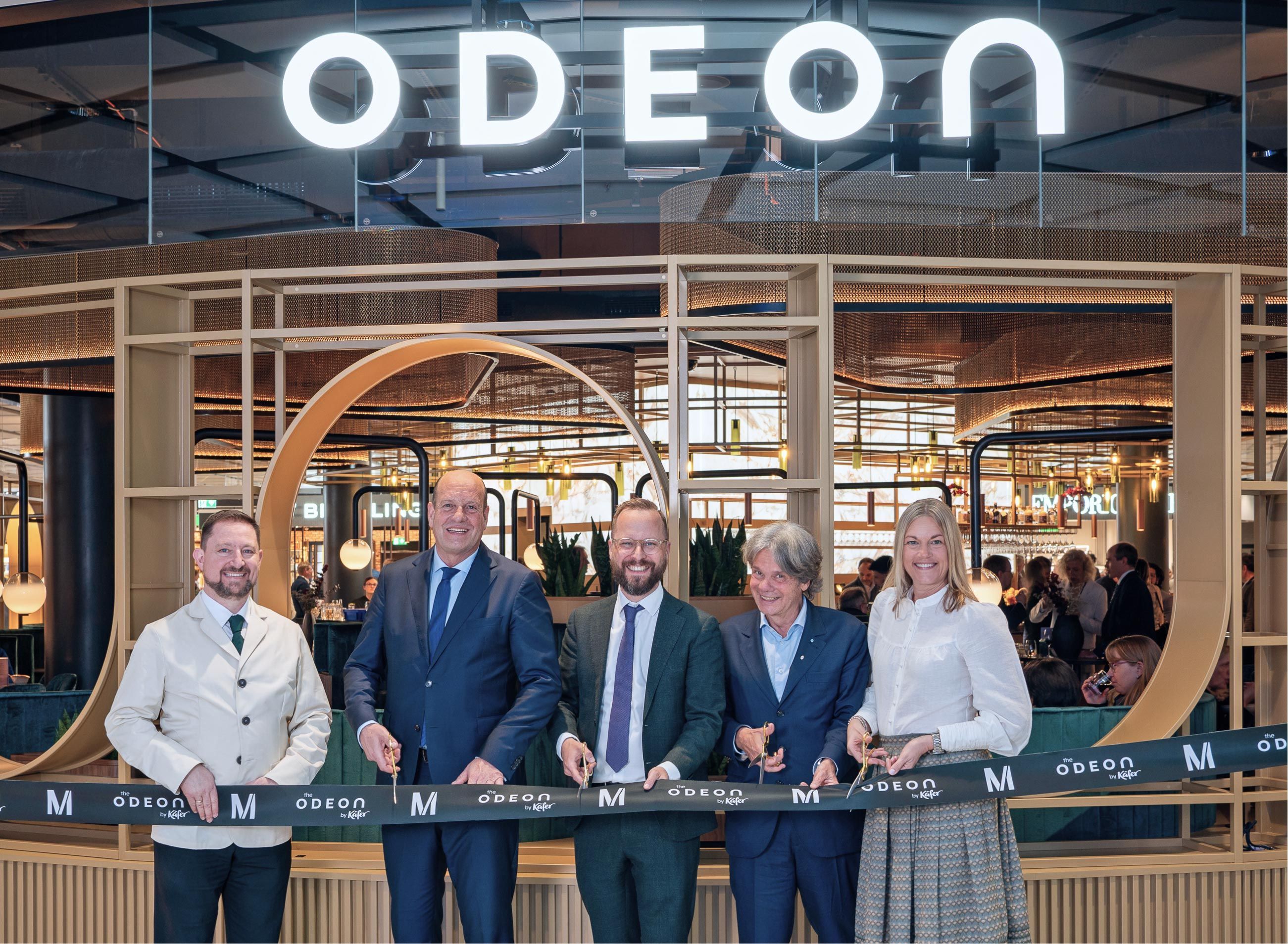 Festive opening of the “the Odeon by Käfer” dining area at Munich Airport: five people together cut a ribbon in front of the illuminated Odeon sign, among them Dr. Jan-Henrik Andersson, Managing Director Commercial and Security.